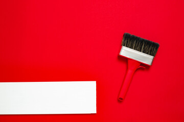 A large new red paintbrush in metal edging with a plastic handle for painting and white wooden plank on a red background. Christmas banner with copy space for a hardware store or art shop