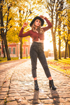 Autumn lifestyle at sunset, blonde Caucasian woman in a red sweater and black hat, enjoying nature in a park with trees. Enjoying the beautiful path of the city park