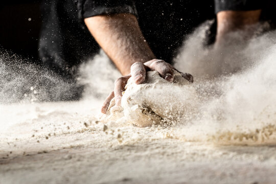 Powdery flour flying into air. chef hands with flour in a freeze motion of a cloud of flour midair. Hands kneading raw dough. Culinary, cooking, bakery concept
