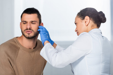 African american doctor in latex gloves checking ear of sick patient