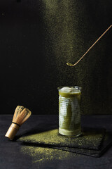 Japanese iced matcha latte and matcha tools on black background.