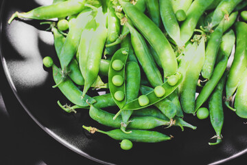 Peas on a black background. Peas in a plate. Summer fruits. Green and black