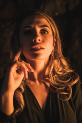 Lifestyle, a young Caucasian blonde in a black dress in a photo inside a cave, illuminated with yellow light. Very seductive portrait of the model