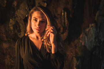 Obraz premium Lifestyle, a young Caucasian blonde in a black dress in a photo inside a cave, illuminated with yellow light. Very seductive pose of the model