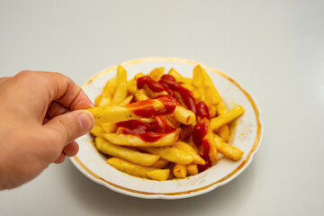 The boy is holding fries that are poured with ketchup and sprinkled with seasoning.