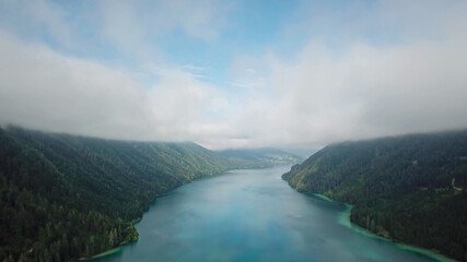 Fototapeta na wymiar Idyllic, drone capture of Weissensee lake in Austria. The lake is surrounded by high Alps. The forest overgrown the slopes. The water has turquoise color. A bit of overcast. Serenity and peacefulness