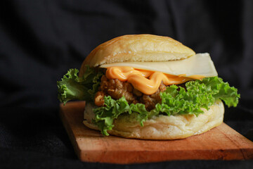 Burger with beef, cheese cream, cheese slice and fresh lettuce on a wooden board with black background