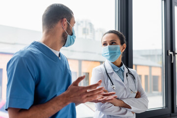 African american doctor in medical mask looking at nurse talking on blurred foreground