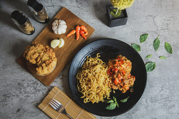 Flat lay, top view. Fried instant noodles with chicken spicy on the black plate and fried chicken on wooden board isolated on grey wall concrete.