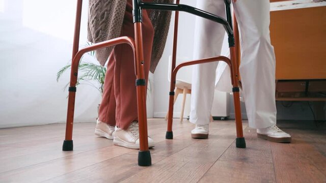 cropped view of aged woman stepping with walkers near nurse
