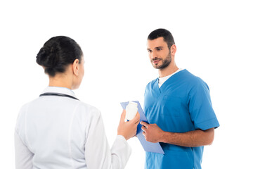 Nurse holding clipboard near african american doctor with jar of pills on blurred foreground isolated on white