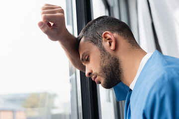 Exhausted nurse standing near window on blurred background in clinic