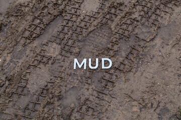 the word mud laid with silver metal letters on wet dirt surface