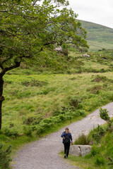 Fototapeta premium A path leads through the park and forest. Girl with backpack hiking towards peak