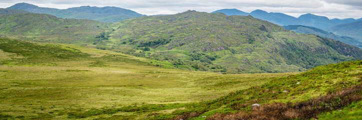 Panoramic view of the Irish countryside with trees, green vegetation, hills and mountains and hills, cloudy day in Ireland
