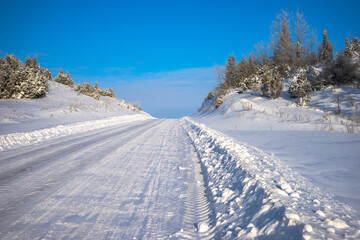 Fototapeta na wymiar Winter road through a forested hill, illuminated by the bright sun. Location Russia, Udmurtia