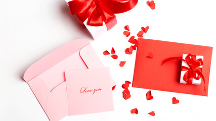 Valentine's Day. Red and open pink envelopes with small cut paper heart and gift box with red bow. Writing a love letter. Message.Top view. copy space. White background. Words I love You