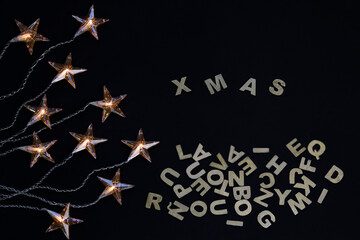 Top view of star shaped Christmas lights and some wooden letters with the word xmas against blackbackground
