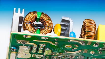 Toroidal electronic inductors soldered on circuit board detail. Copper wire coil winding. Electric components and aluminum cooler in voltage converter of dismantled computer power supply. Bottom view.