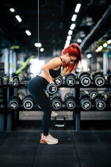 Portrait of attractive caucasian woman working out int the gym, using barbell and dumbbells