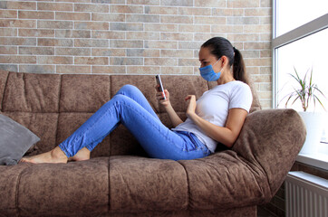 A woman in a mask with a phone on the couch