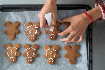 Anonymous woman decorating some homemade gingerbread men cookies at kitchen