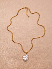 Luxury elegant baroque pearl pendant with golden chain on beige leather background