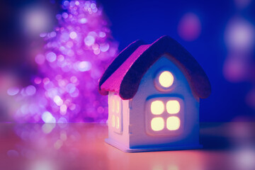 Toy house with glowing windows over defocused lights of Christmas tree