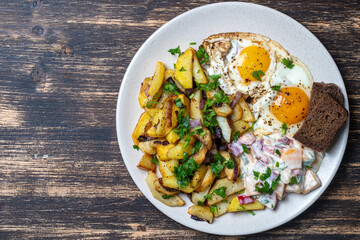 Ukrainian food, fried potatoes with onions, eggs, vegetable salad, black bread on wooden background