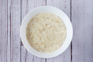 Oatmeal porridge in a deep white plate, top view.