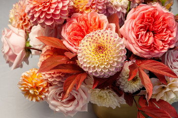 Floral composition of dahlia flowers, roses and autumn leaves. Arty, bright red and pink color  bouquet of flowers on gray concrete background 