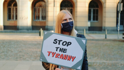 Young woman in protective mask calling to stop the tyranny by holding steamer. Protest walk in the city center.