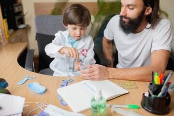 Little boy playing pretends like doctor examining a man in comfortabe medical office. Healthcare, childhood, medicine, protection and happiness concept. Having fun, laughting while giving pills