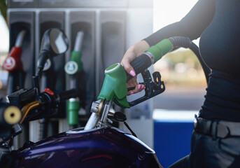 Female's gentle hand is holding a fueling gun. Motorcycle's tank is fueling by female owner.