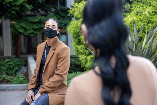 Two African American Women Wearing Masks To Protect From The Covid-19 Coronavirus Sit 6 Feet Apart For Social Distancing While Talking