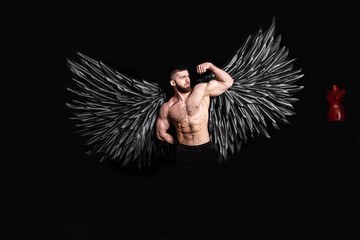handsome muscular man in angel costume with black wings on black background
