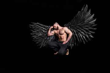 handsome muscular man in angel costume with black wings on black background