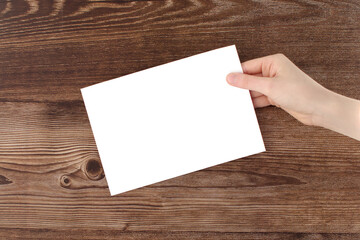 Ad. Text. Advertising. Copy space. Logo. An empty sheet of white paper in a hand on a wood background.