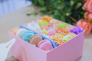 Close up view of gift box with flowers and colorful macaroons at flower shop. Floristry, handmade, wedding, birthday, dessert, biscuit, sweet food and traditional french cuisine concept
