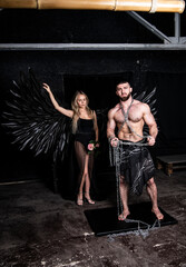 beautiful girl in angel costume with black wings and handsome muscular man struggling with difficulties on a black background