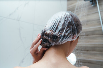 Back view. Woman puts a shower cap on her hair