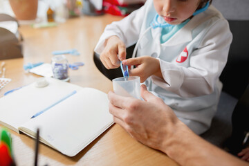 Little boy playing pretends like doctor examining a man in comfortabe medical office. Healthcare, childhood, medicine, protection and happiness concept. Having fun, laughting while giving pills