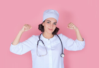 A beautiful female doctor in uniform with a stethoscope demonstrates a winning gesture, strength. Isolated on a white background. The concept of medicine and health care in the fight for health