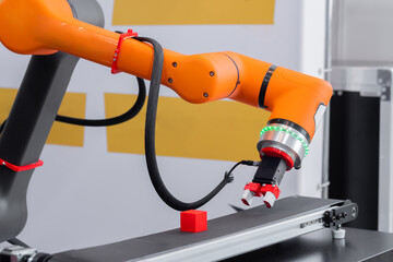Orange pick and place robotic clamp arm manipulator moving red toy blocks at modern robot trade...