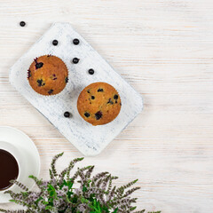 Cupcakes with black currants on a white wooden cutting board against the background of a cup of tea. View from above.