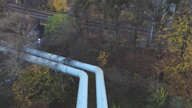 Large pipes of the heating main on a cloudy sunset.
View from above. At the bottom, there are green areas, trees, bushes and grass.