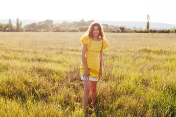 Naklejka na ściany i meble Portrait of a beautiful fashionable woman in a yellow dress in a field at sunset
