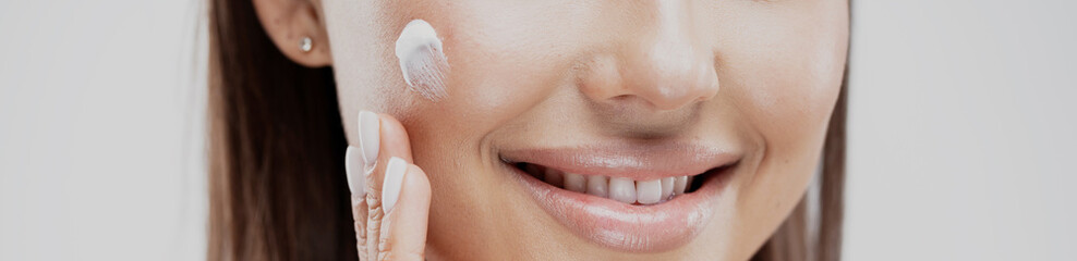 Naklejka premium the woman smiles and shows even white teeth. apply face cream to clean skin. refreshing cleansing women's cosmetics. white color nail art manicure