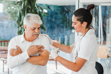 hispanic woman nurse injecting vaccine into senior patient's arm