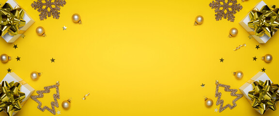 Xmas decoration. White gifts with golden bow, yellow balls and sparkling lights in Christmas decoration on yellow background for greeting card. Flat lay, top view, copy space.